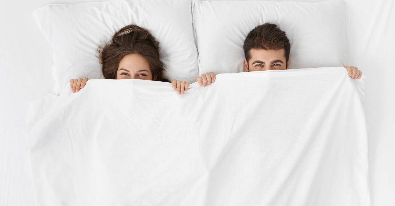 En kvinna och en man gömmer sig under ett täckeoch ser busiga ut
