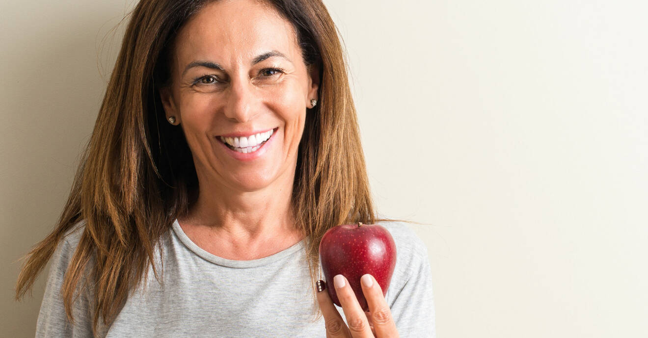 Kvinna ler och håller upp ett äpple mot kameran