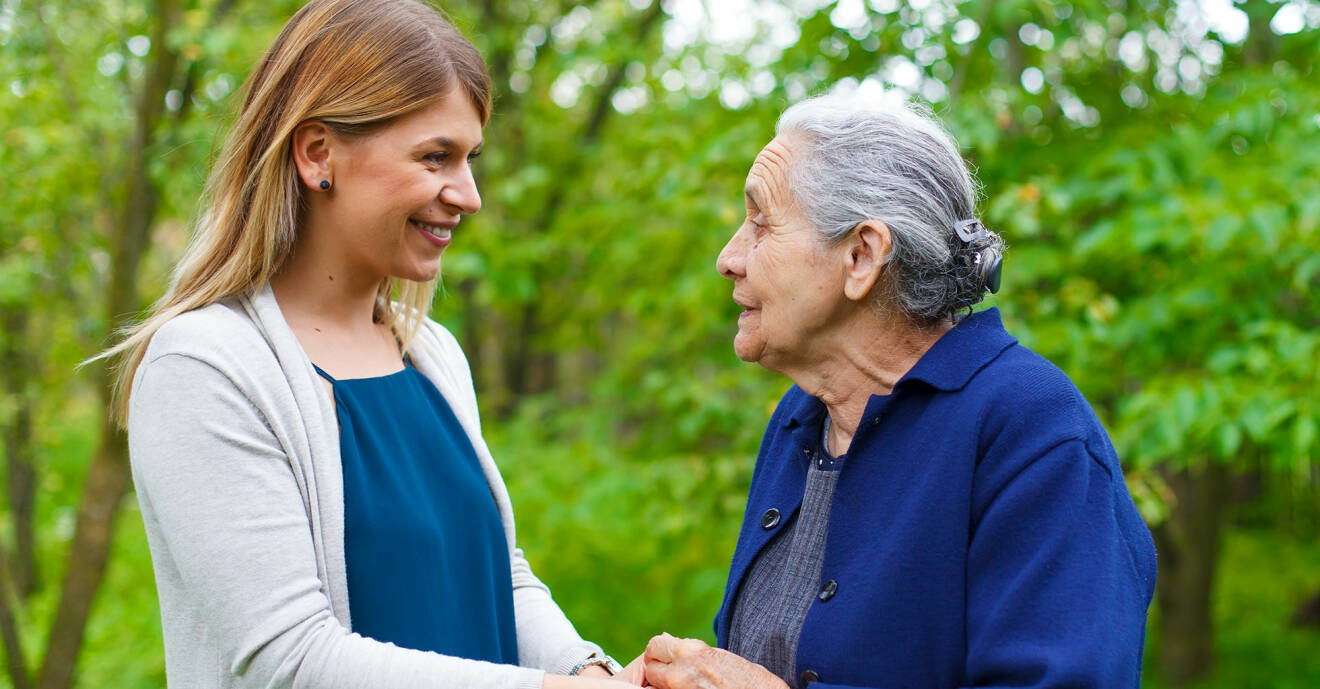 Kvinna håller en äldre dement kvinna i handen