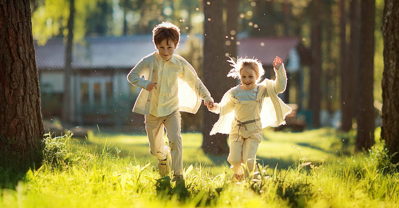 Två barn springer och leker i en lummig trädgård
