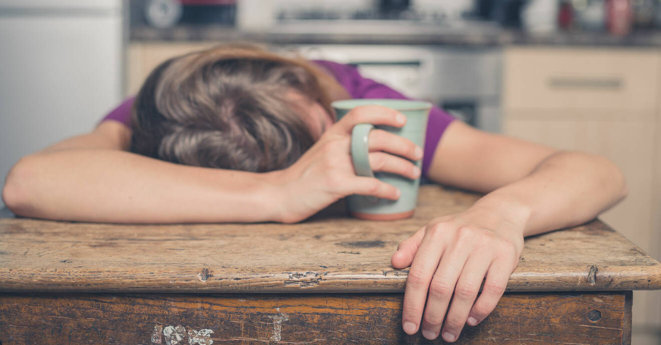 Utmattad kvinna hänger över ett köksbord