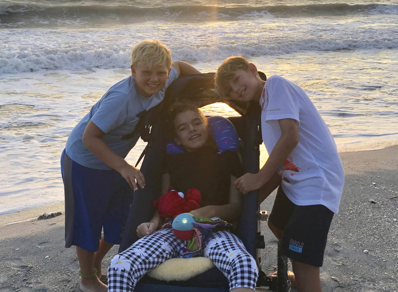 Alicia tillsammans med sina bröder Damien och Liam på en strand med solnedgången i bakgrunden. 