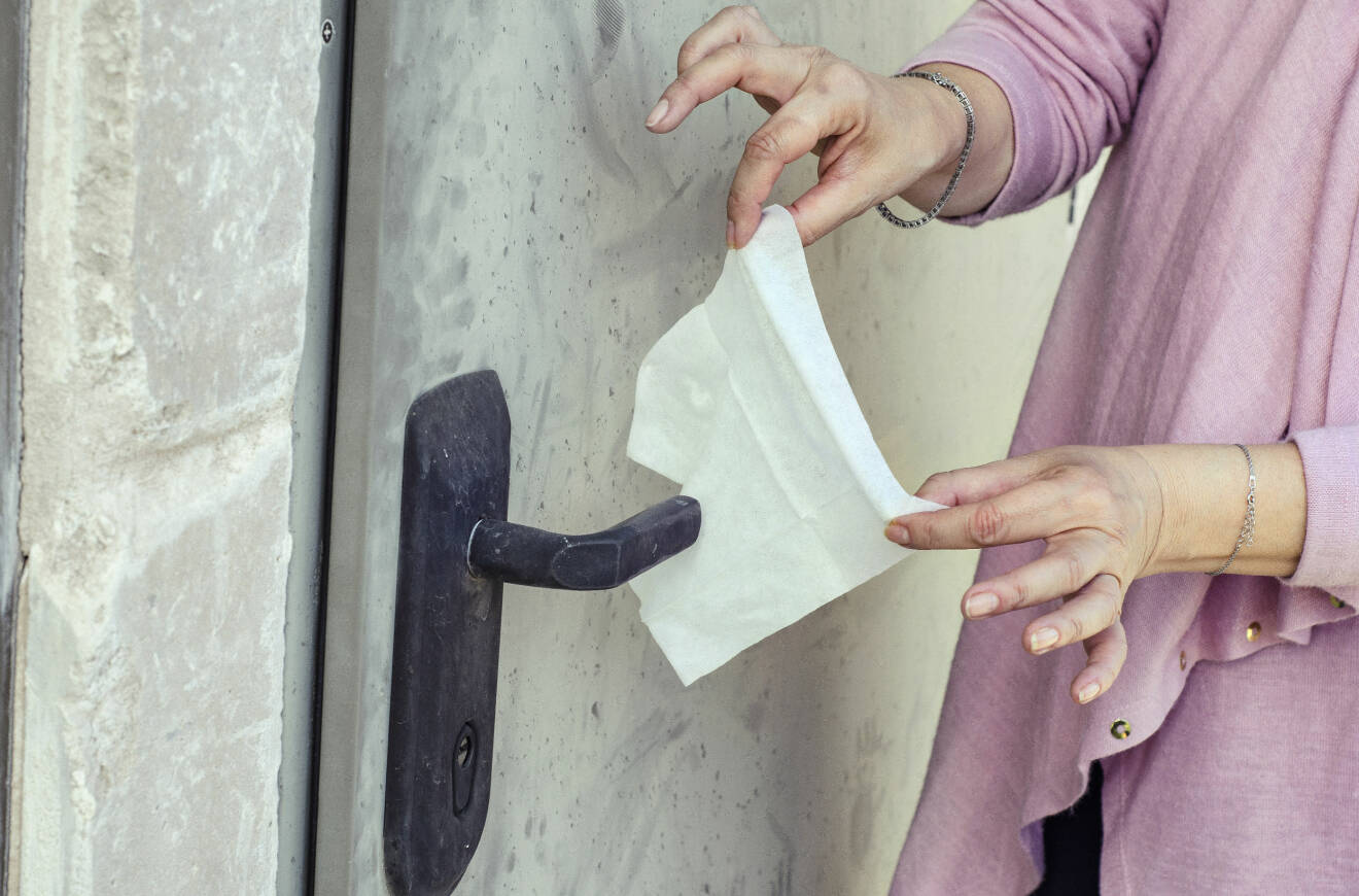 Kvinna torkar ett dörrhandtag med en servett.