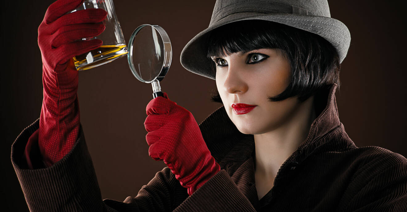 En kvinnlig detektiv undersöker ett glas med förstoringsglas.