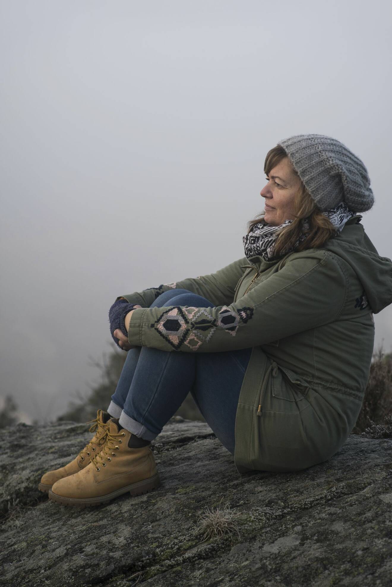 En kvinna i övre medelåldern sitter med varma kläder på en klippa och ser nöjd ut.