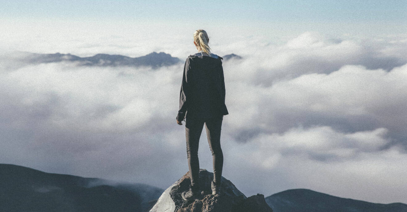 Emma står på en bergstopp och blickar ut över molnen.
