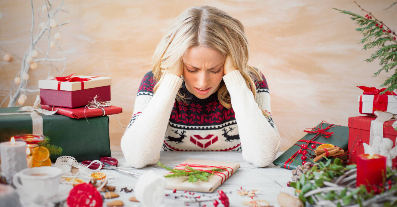 Stressad kvinna sitter vid ett bord och stirrar på julpynt och julklappar.