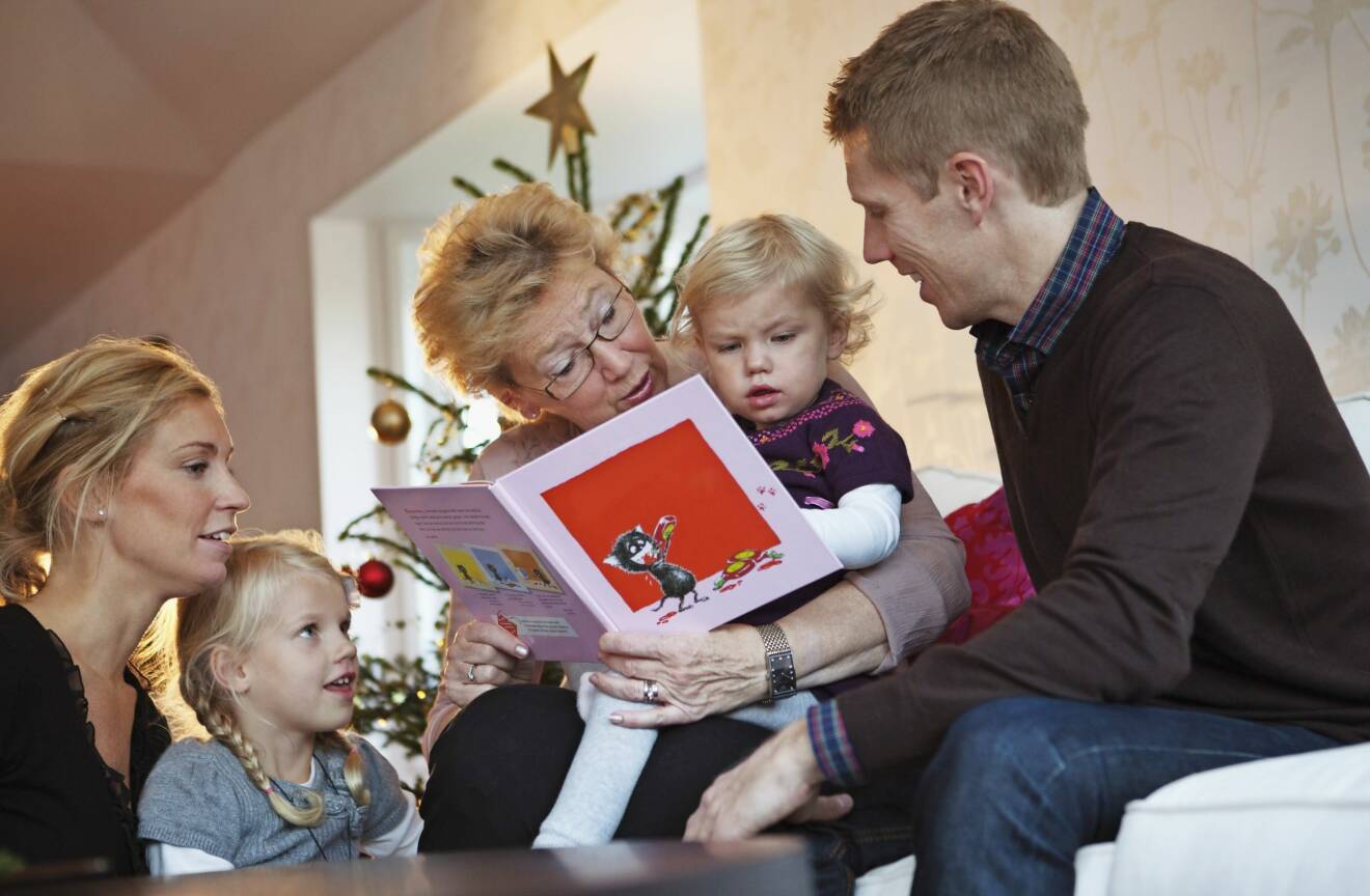 Familj sitter tillsammans framför en julgran och läser en bok.