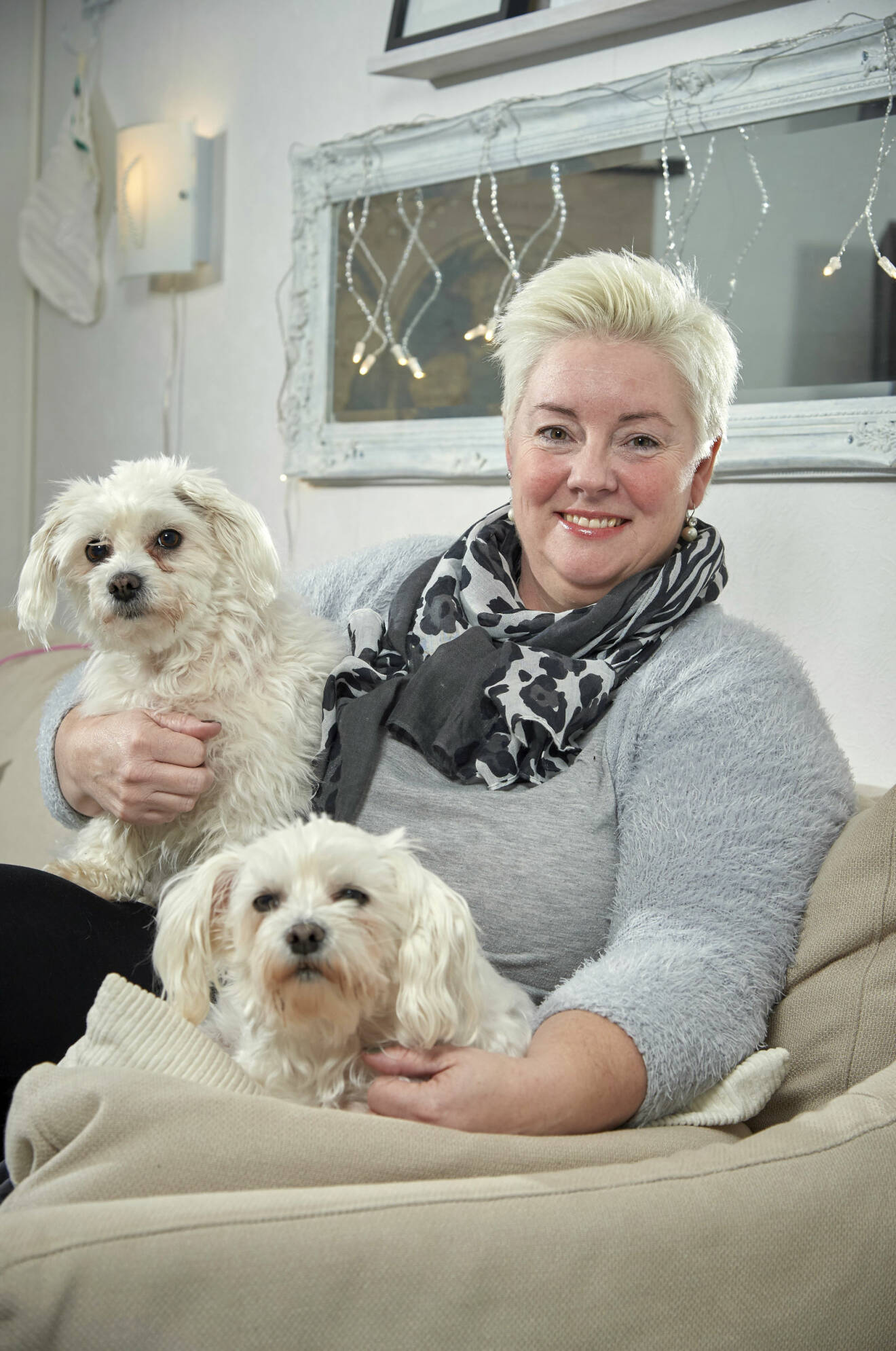 Ulrika kvinna sitter i soffan med två malteser-hundar i knät.