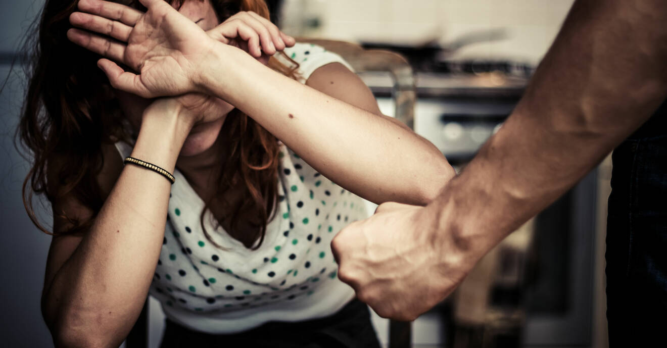 Kvinna håller upp händerna för att värja sig mot mannens knutna näve.