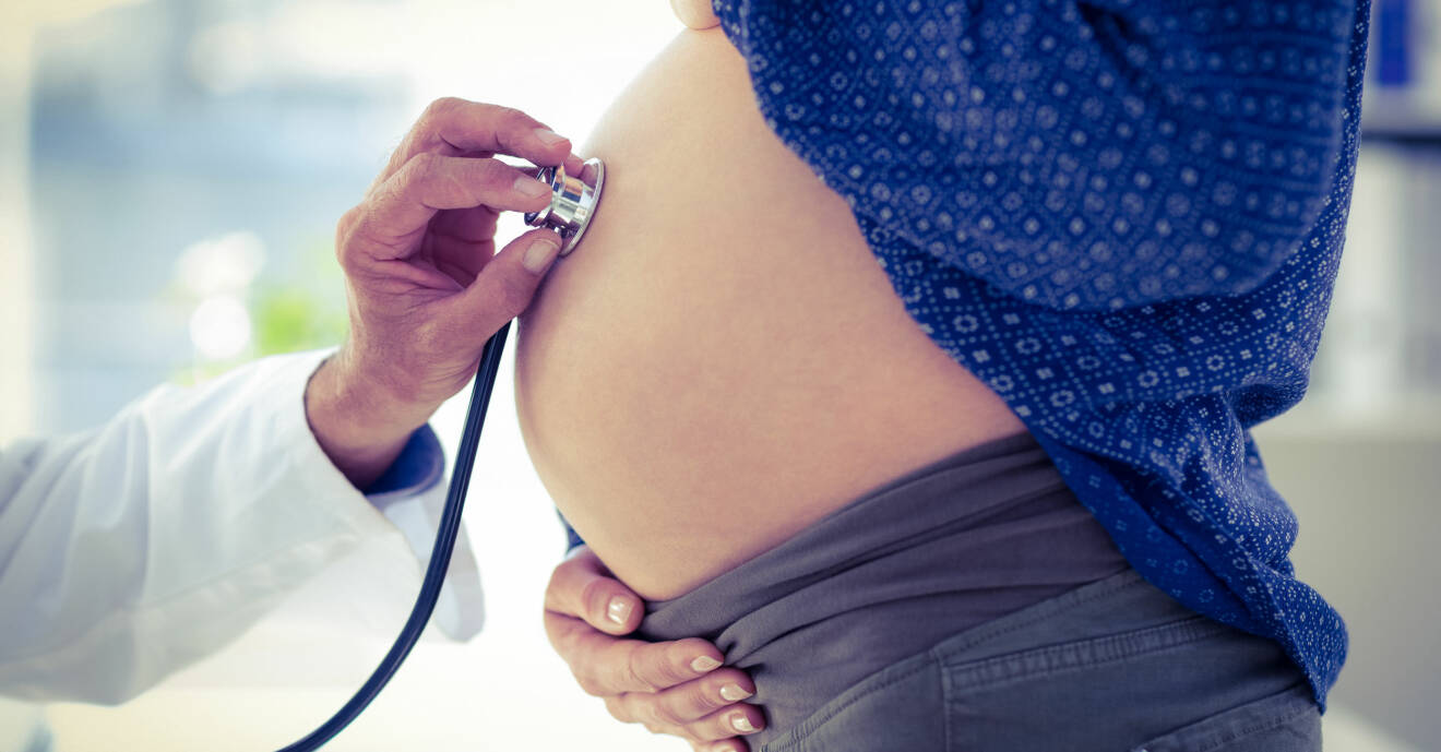 Gravid kvinna på hälsokontroll hos läkaren som lyssnar med stetoskop.
