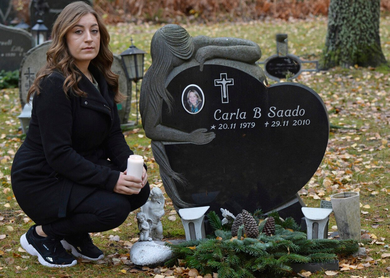 Carla besöker sin mamma Carlas grav. Jennifer sitter på huk på kyrkogården bredvid sin mamma Carlas gravsten som är formad som ett hjärta och där det finns en porträtt av mamman