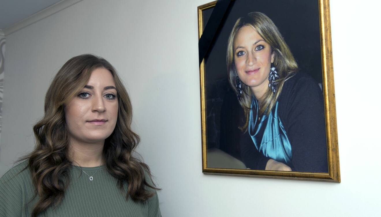 Jennifer står vid en vägg där det hänger ett inramat foto av hennes mamma Carla.