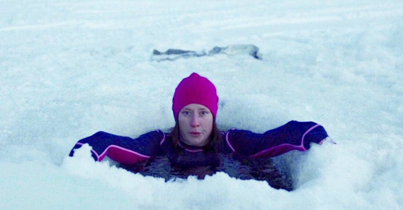 Petra tittar upp ur en isvak, iförd i kläder och mössa medan hon badar.