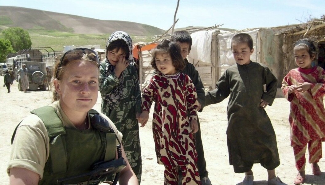 Barnen i byn var nyfikna på Petra. Foto: Privat Soldaten Petra sitter på huk i en afghansk by, fem barn står intill.