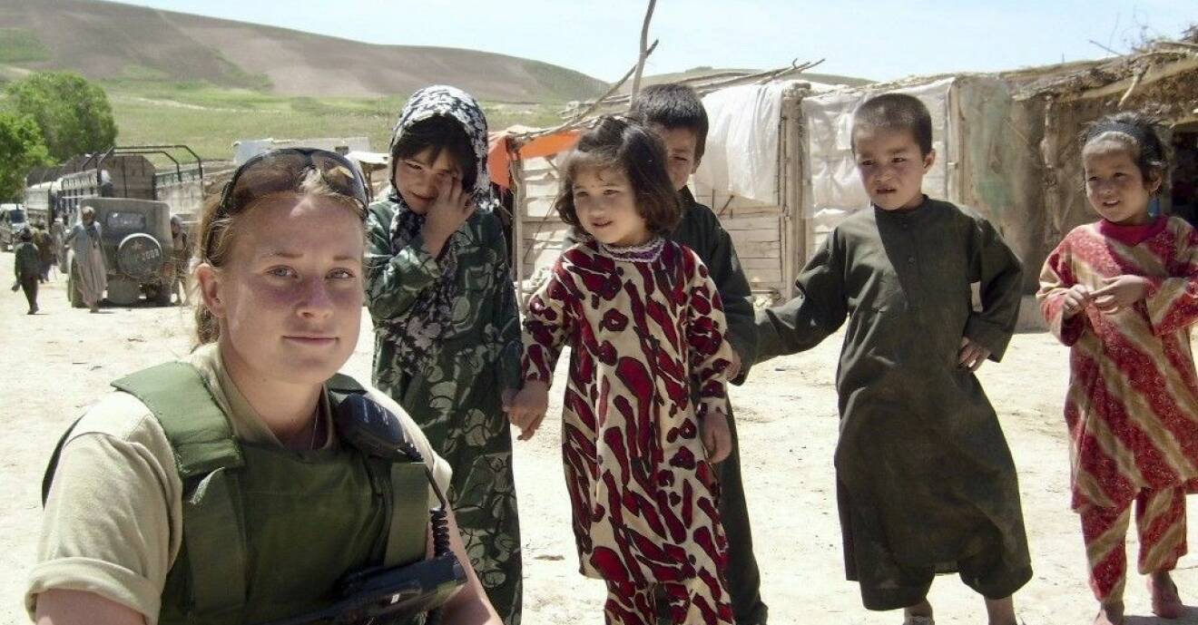 Soldaten Petra sitter på huk i en afghansk by, fem barn står intill.