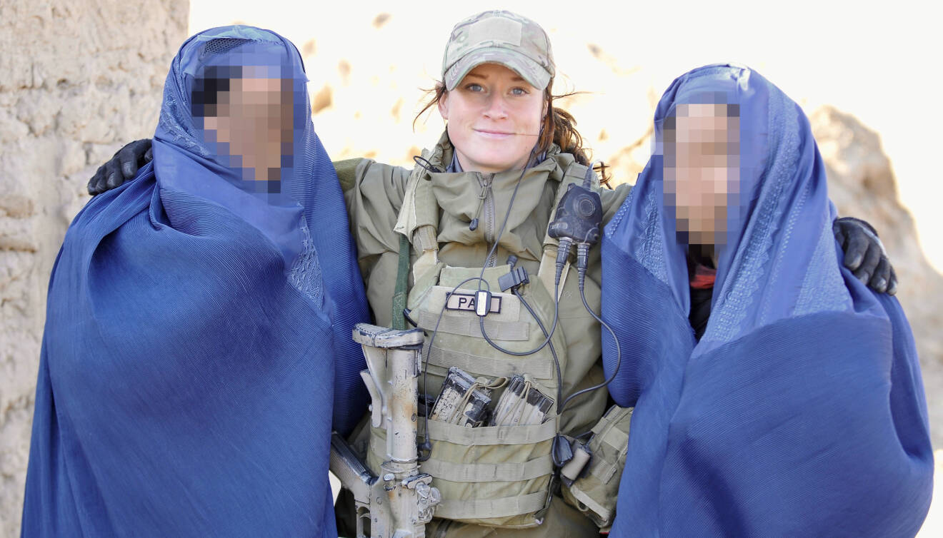 Petra i uniform mellan två maskade kvinnor i stora blå slöjor.