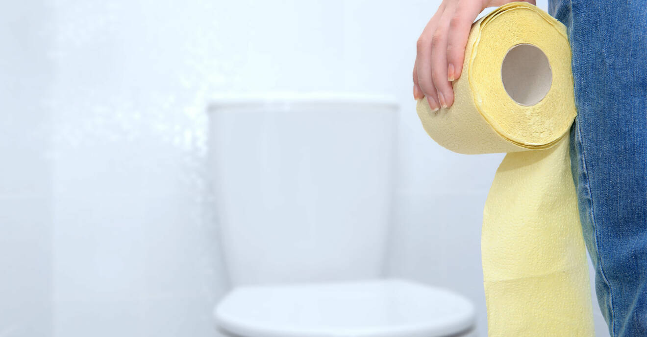 Kvinna på toalett med en rulle gult toalettpapper i handen.