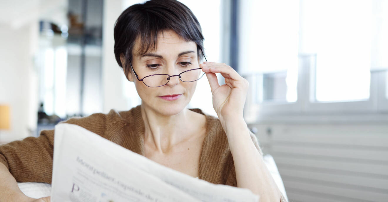 Kvinna med glasögon läser tidningen.