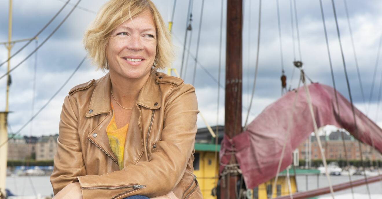 Ann sitter i hamnen i Stockholm och bakom henne syns båtar och hus.