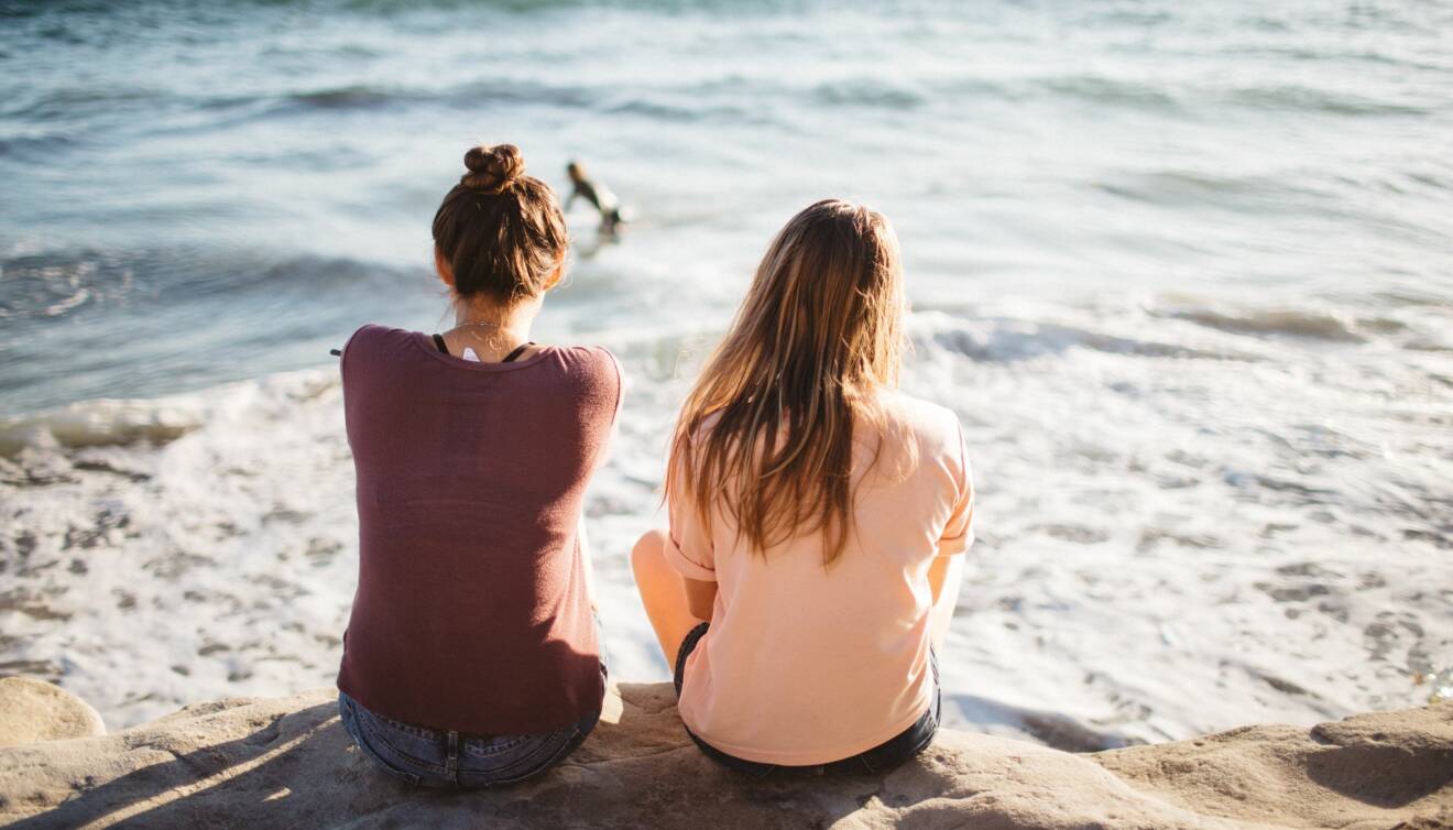 Två vänner sitter tillsammans på en strand.