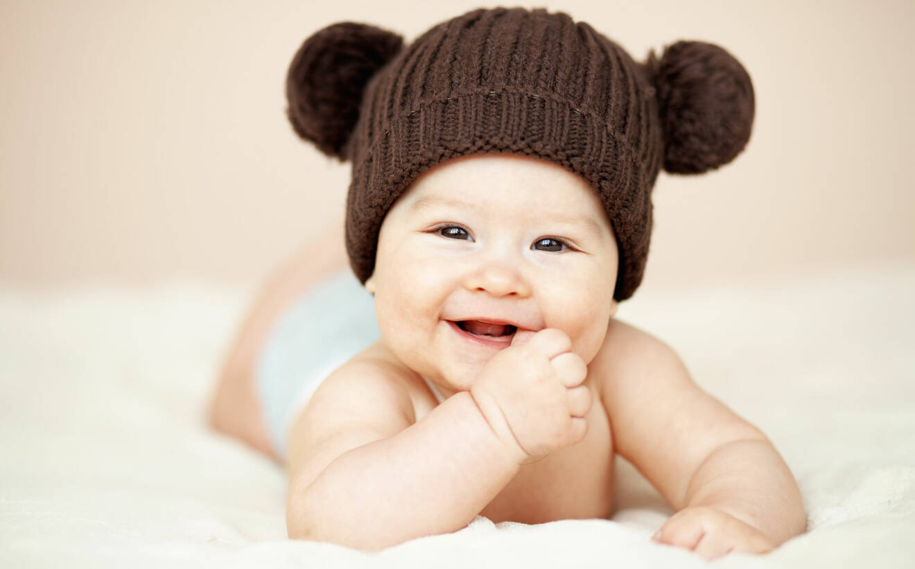 Bebis med brun mössa ler mot kameran.