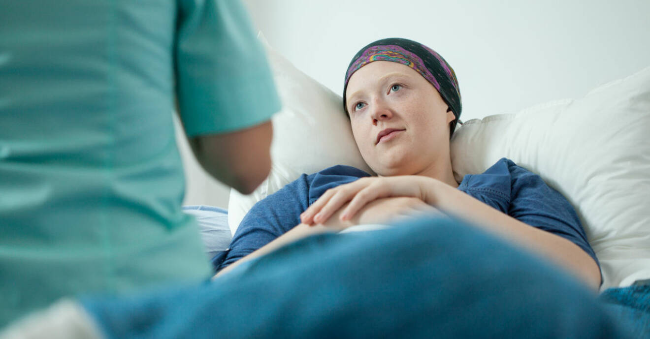 Kvinna sjuk i cancer ligger i en säng och tittar upp på läkaren.