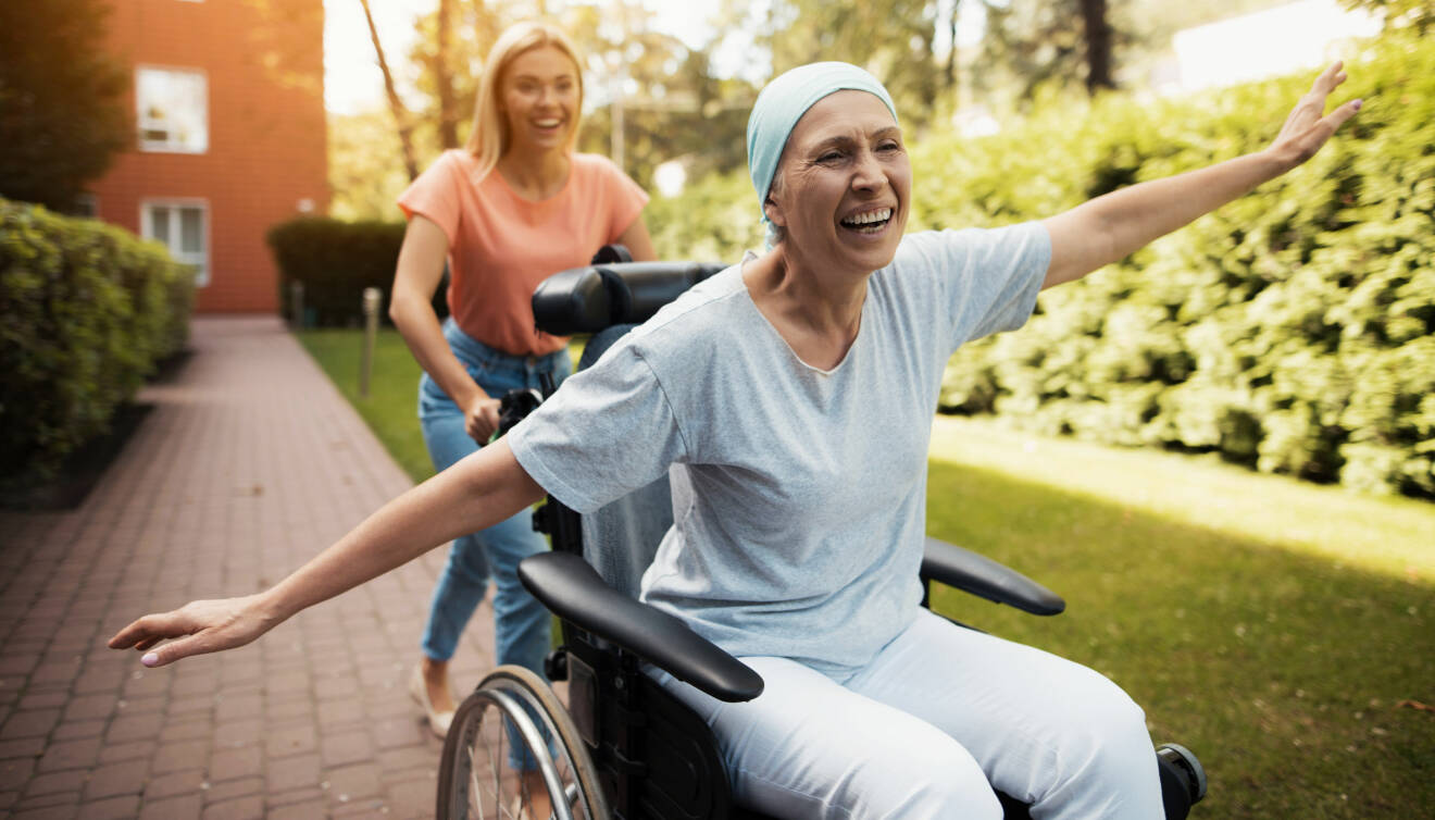 Cancersjuk kvinna blir körd i rullstol av yngre kvinna.