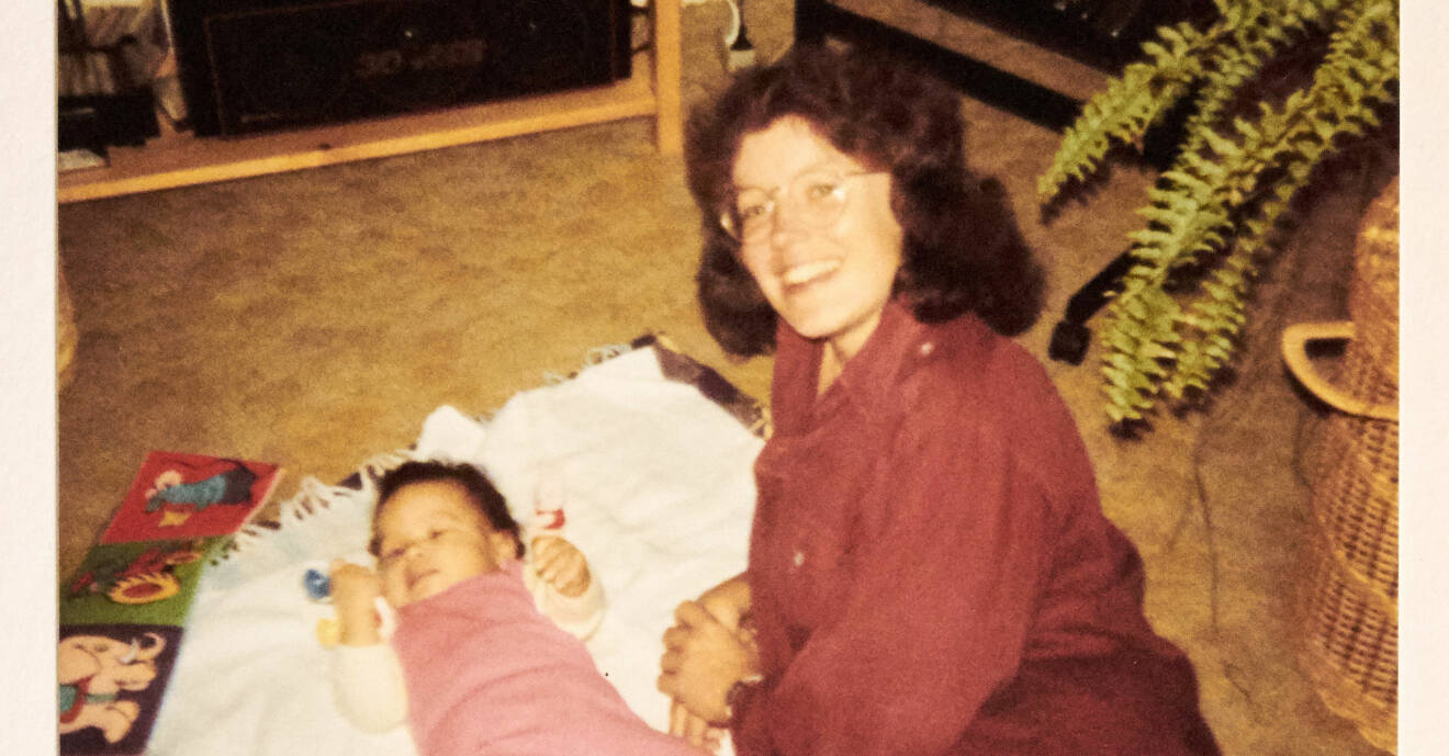 Lilla babyn Kirstine ligger på en filt på golvet och mamma Anne-Marie ler mot fotografen.