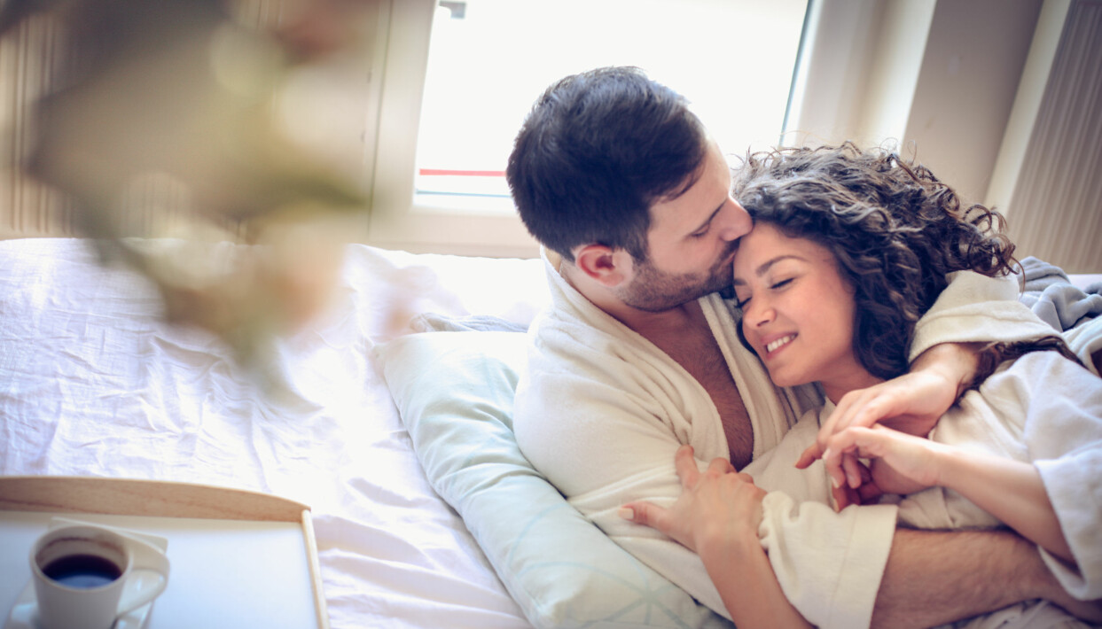 Överraska din partner med frukost på sängen! Foto: Shutterstock/TT Man och kvinna ligger och gosar i en säng med en frukostbricka vid sidan.
