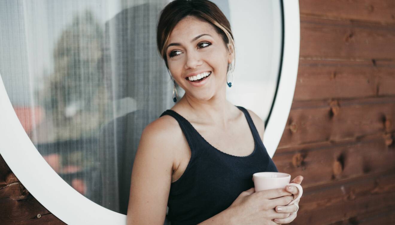 Kvinna står med en kopp kaffe i handen och ser avslappnad ut.