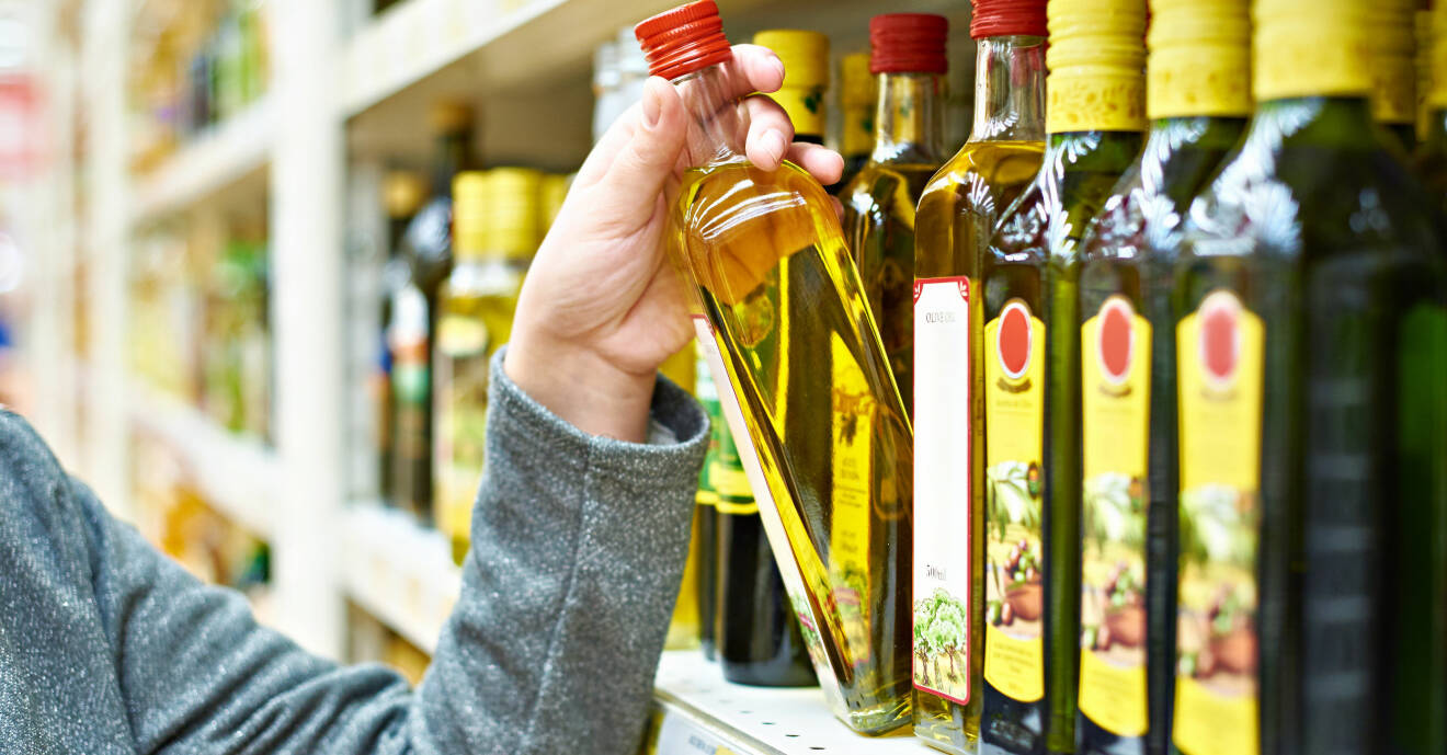 Kvinna plockar ner en flaska olivolja från en butikshylla.
