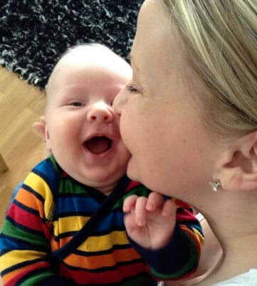 Suvi och sonen Valter när han var bebis. Suvi håller sin bebis Valter och pussar honom på kinden och han ler ett tandlöst leende.