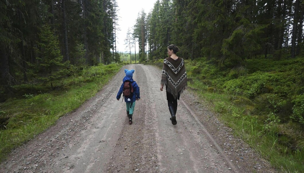 Skogspromenad i gemenskap. Mor och barn på promenad på en liten skogsväg.