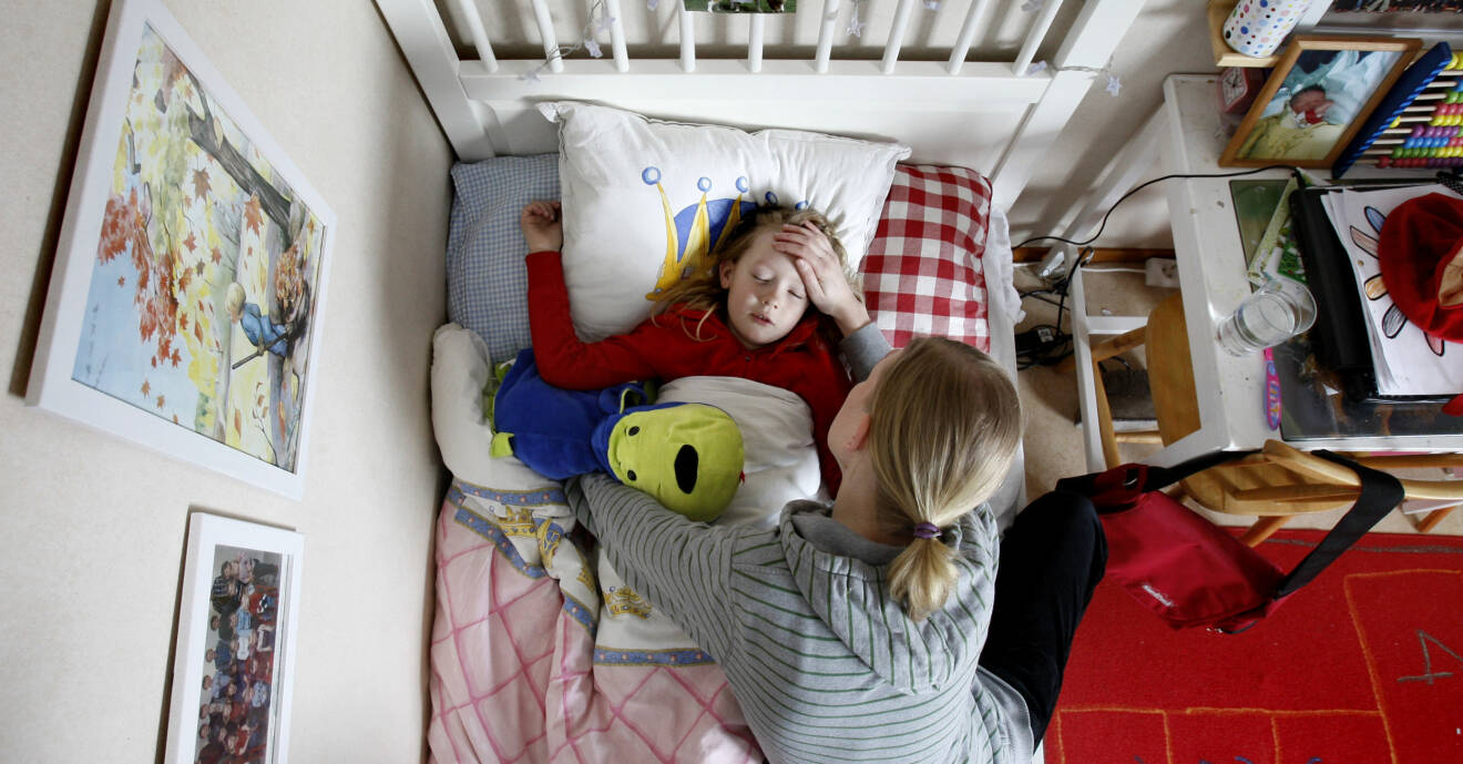 En kvinna håller handen på pannan på ett sjukt barn som ligger i sängen