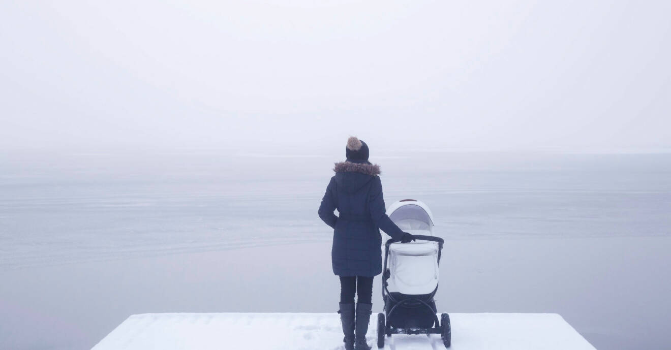 En kvinna med barnvagn står och tittar ut över havet i vintertid.