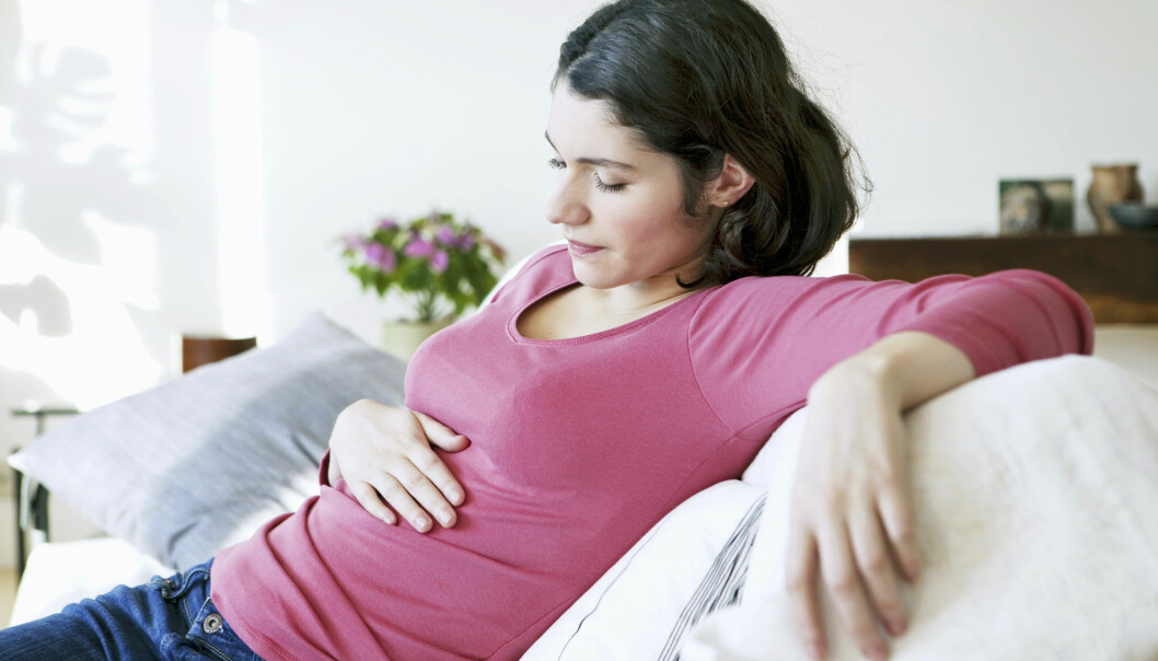 Var uppmärksam på diffusa symtom, som uppsvälld mage. Foto: Shutterstock/TT Kvinna i soffa som håller en hand på magen.