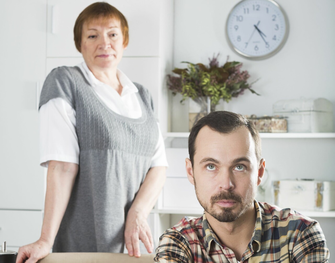 Man sitter vid ett bord och himla mer ögonen åt sin mamma som står bakom honom.