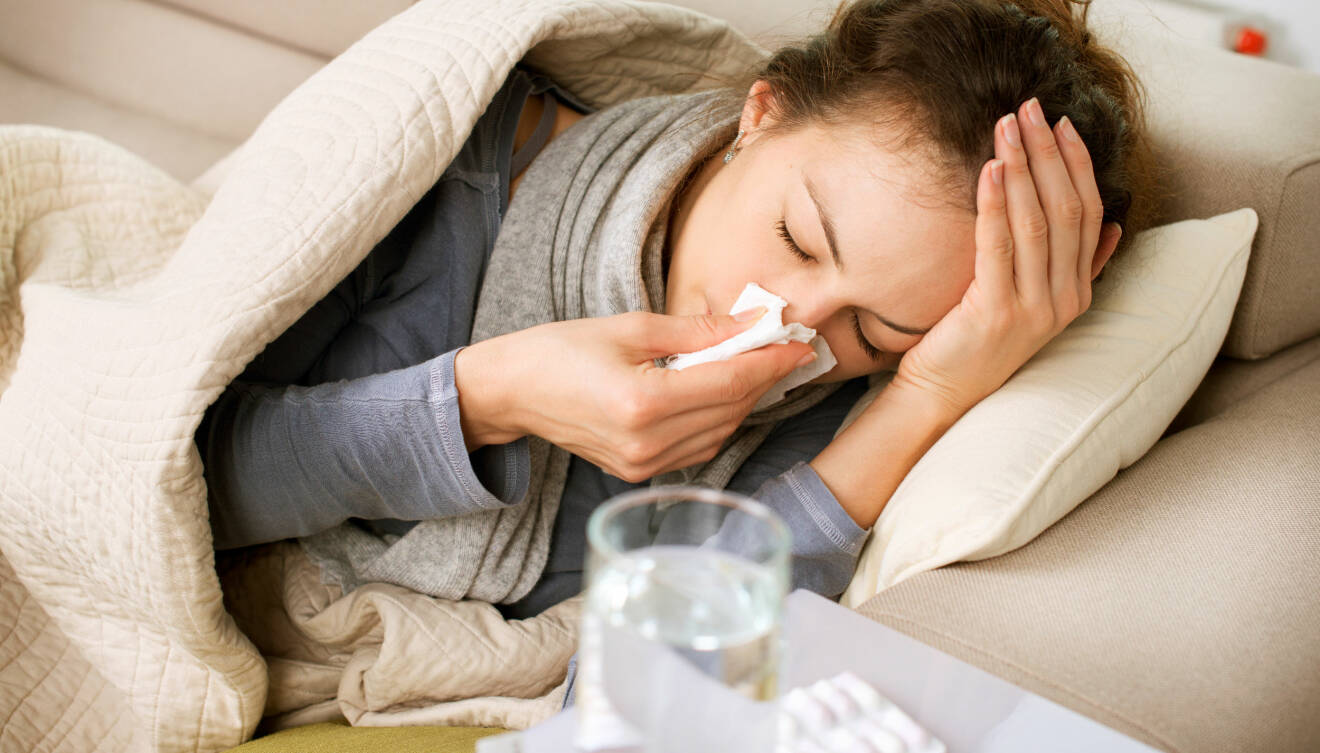 En kvinna ligger i soffan med influensasymtom.