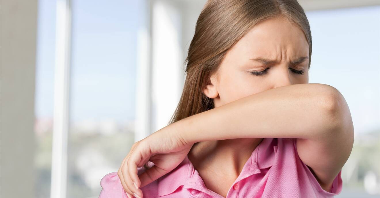 En kvinna nyser i armvecket för att inte sprida coronavirus.