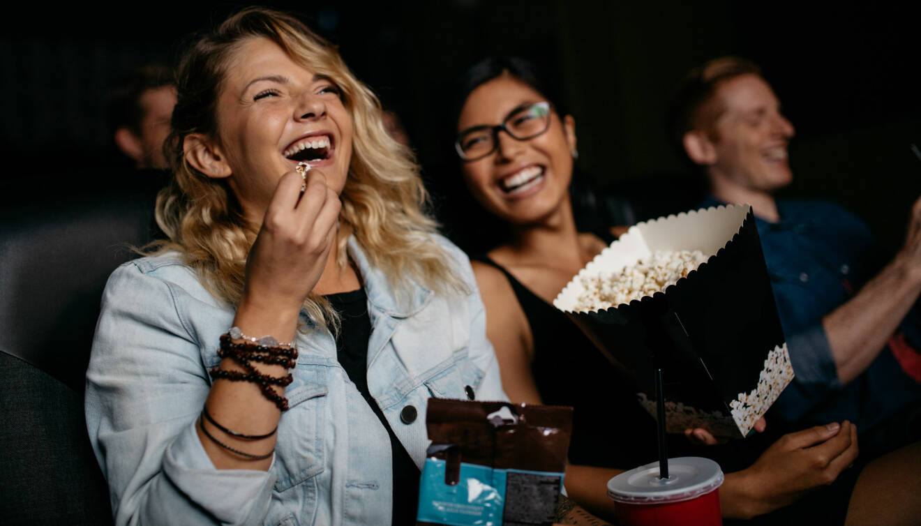 Kvinnor skrattar tillsammans under en film på en biosalong.