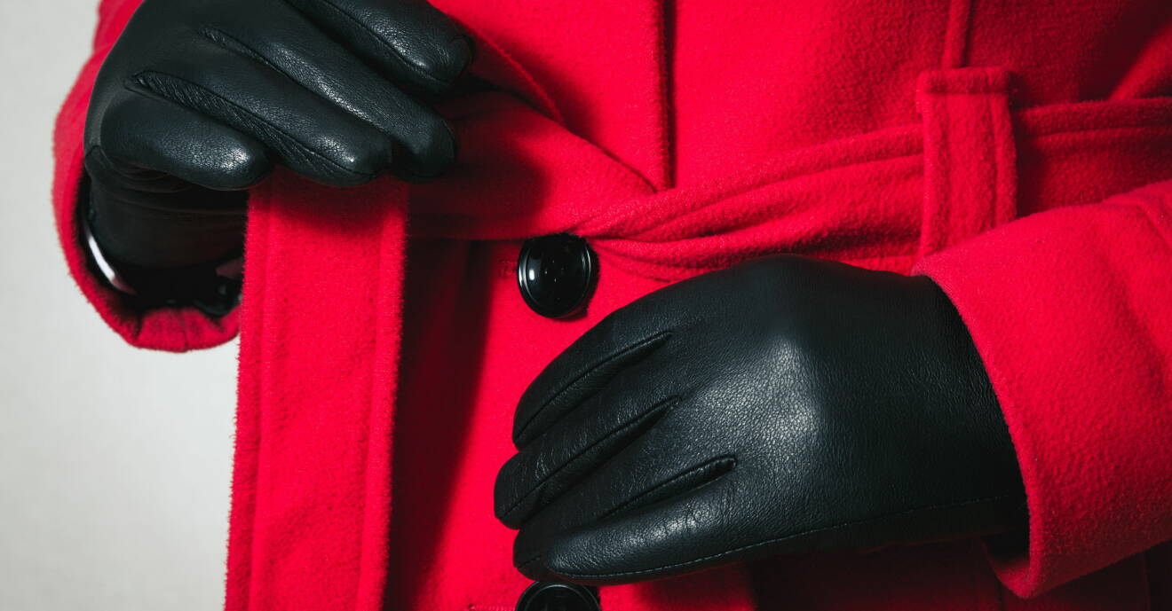 Kvinna med handskar knyter ett skärp runt sin kappa med svarta knappar.