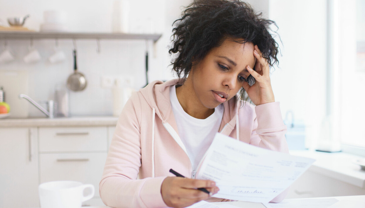 Tusentals människor har redan sagts upp till följd av coronakrisen. Kvinnodominerade yrken är hårt drabbade. Foto: Shutterstock/TT En kvinna sitter vid sitt köksbord och tittar oroligt på några papper.