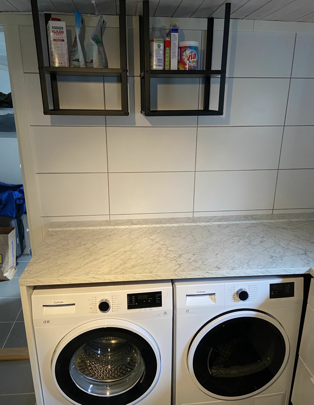 Inga plugg behövdes för att skruva upp Ikea-borden eftersom taket är i trä. Foto: Privat Två metallbord från Ikea är fastskruvade i ett trätak och fungerar nu som hyllor för tvättmedel.
