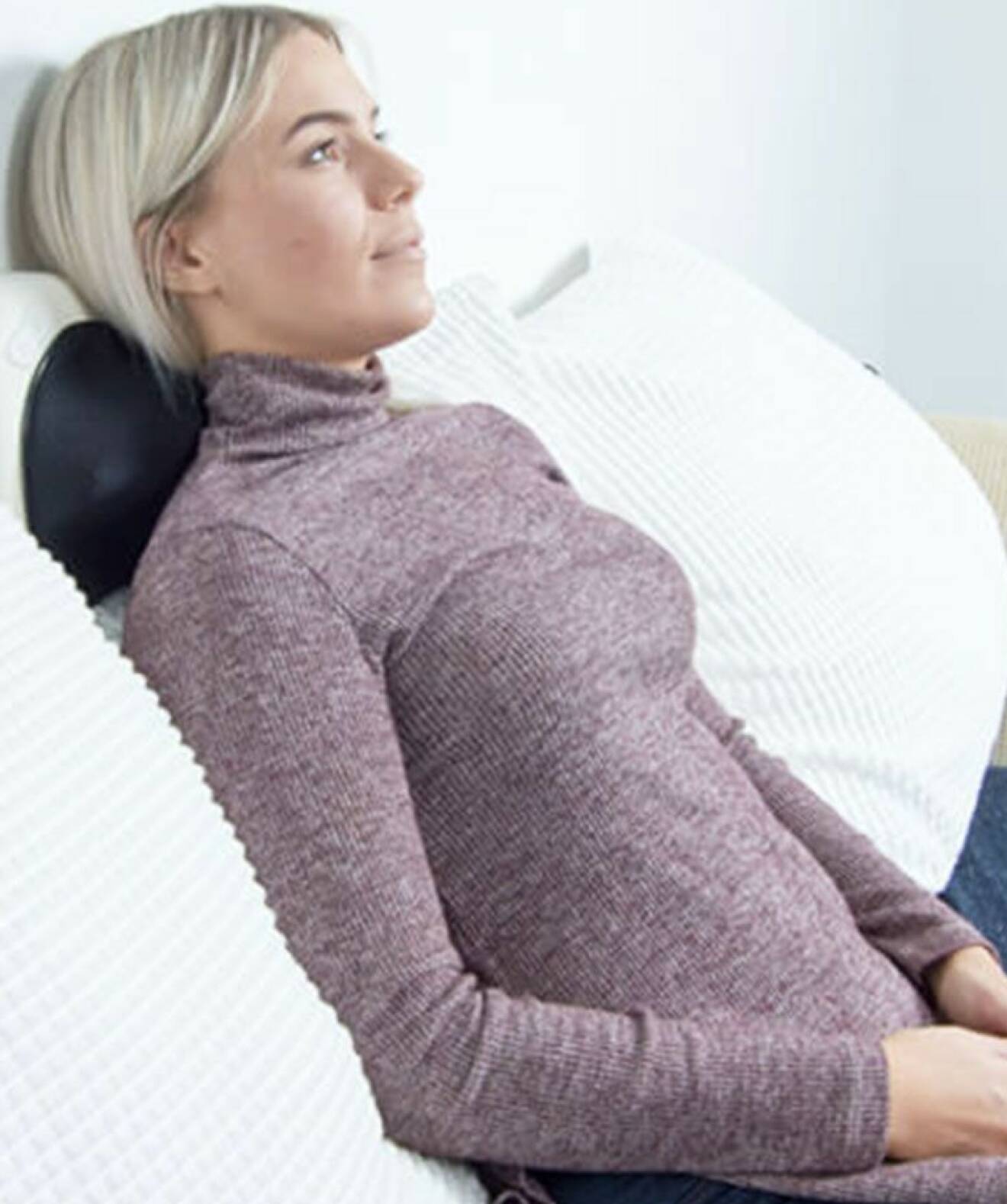 Kvinna sitter i soffan och får massage av en massagekudde.