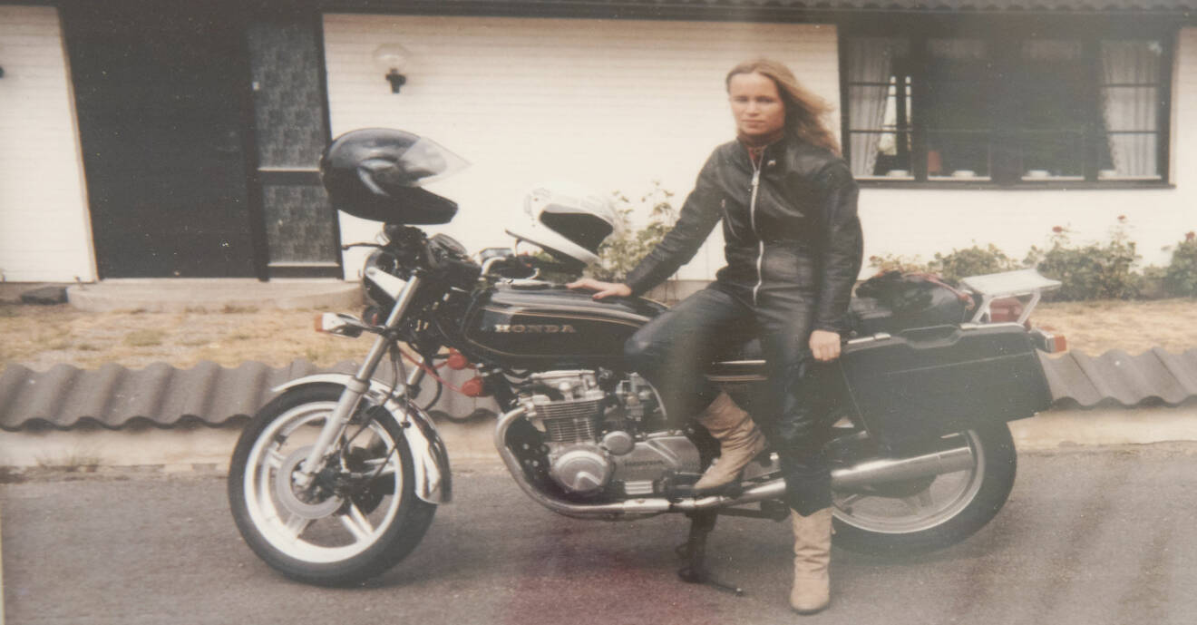 En ung Carin i svart skinnställ poserar framför en svart motorcykel.
