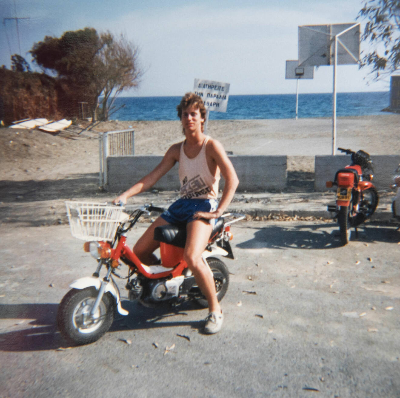 Micke som ung sitter på en moped i linne och shorts och i bakgrunden syns havet.