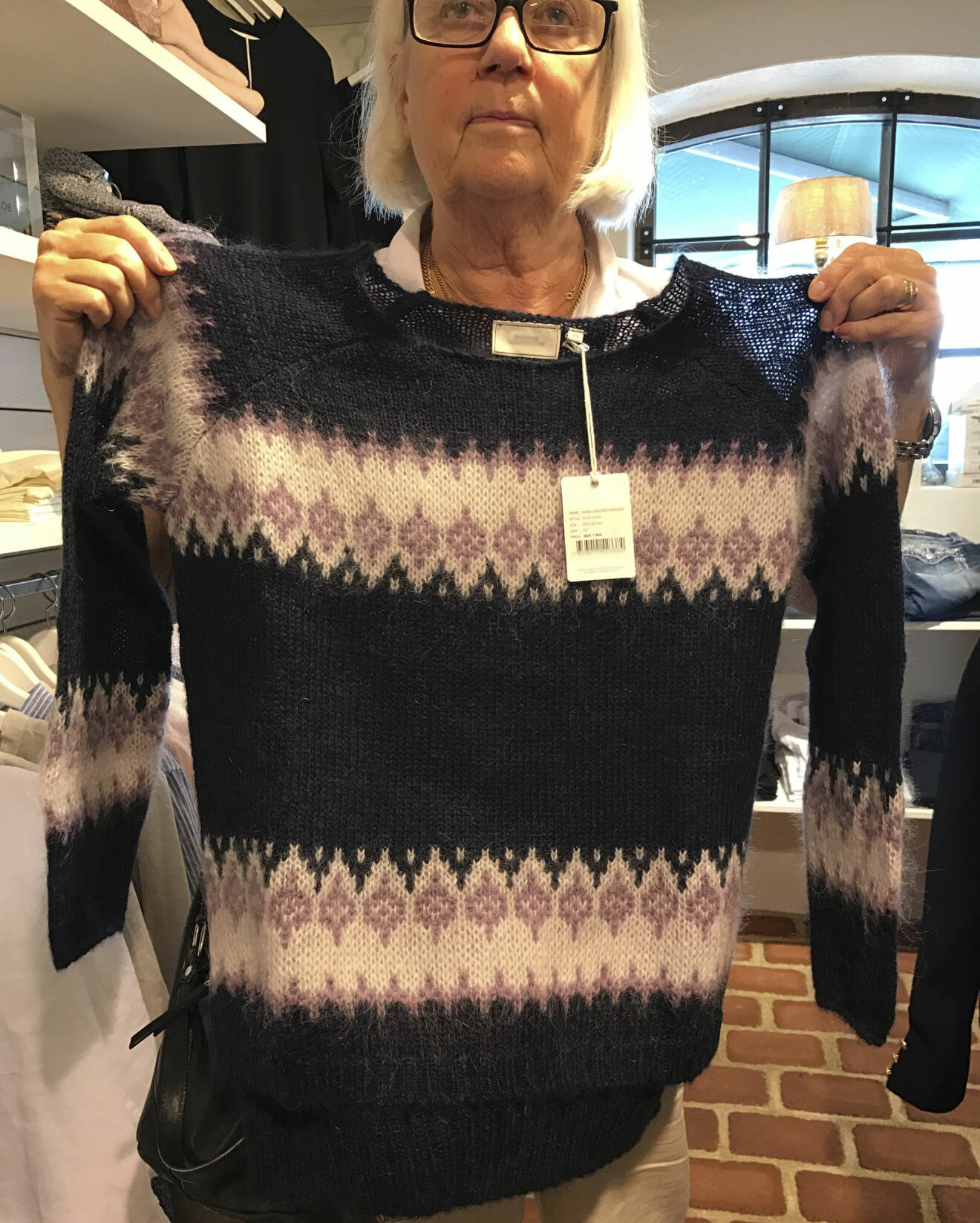Helen, 75 år, står i en butik och håller upp en stickad tröja med mönster