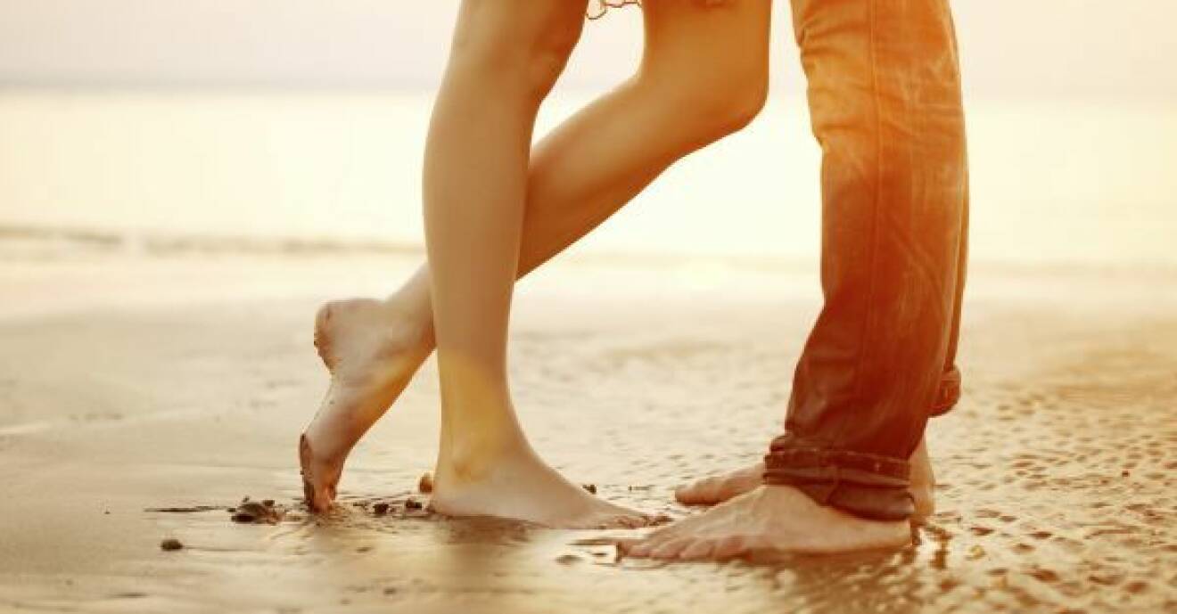 Två par fötter står nära i sanden.