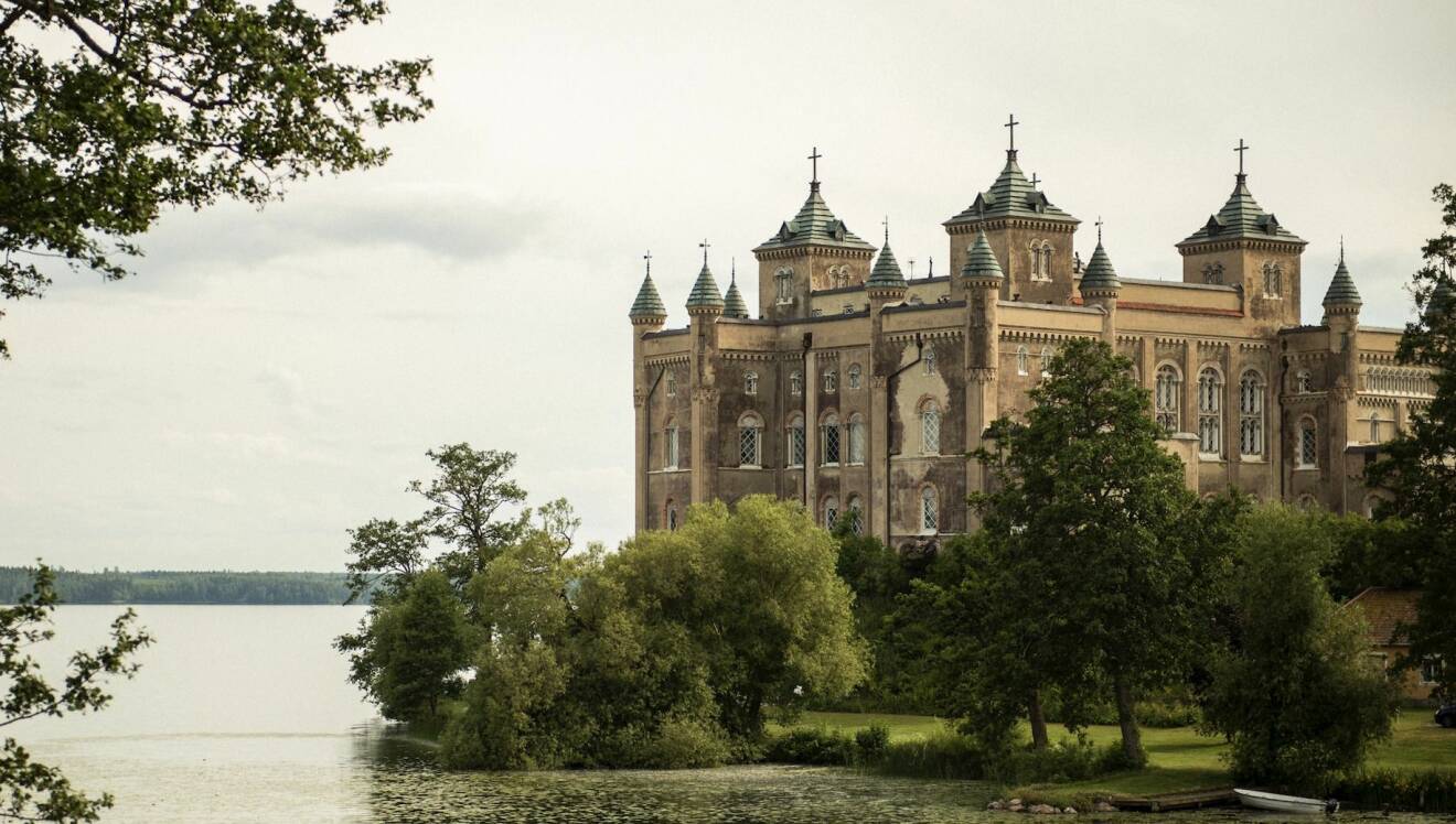 Stora Sundby slott, omgivet av träd och kullar precis intill kanten av Hjälmarens vatten.
